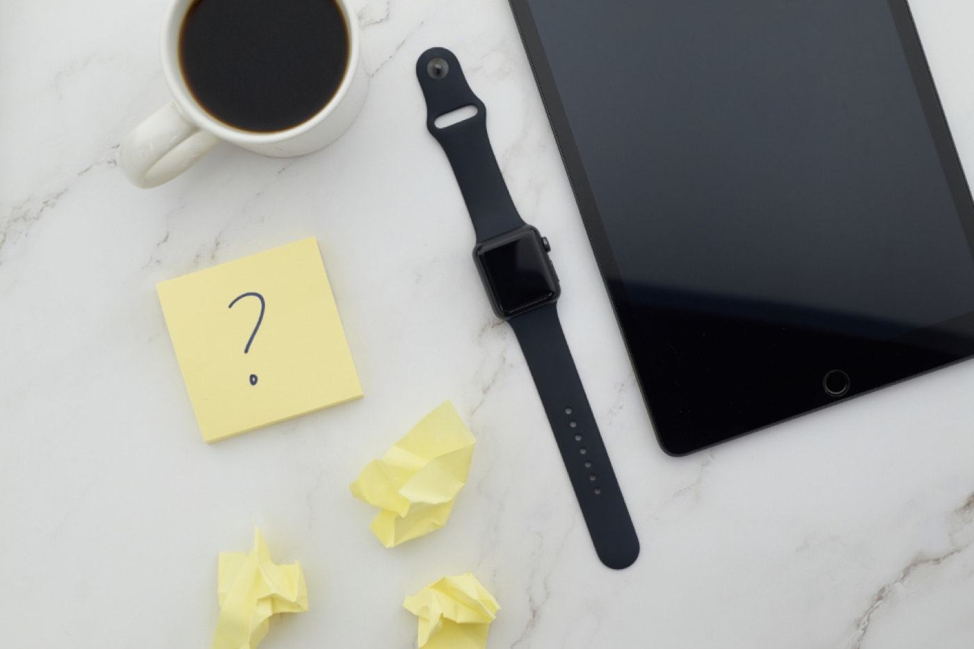 A question mark on a sticky note beside a coffee and a tablet